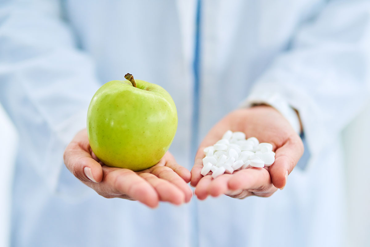 Arzt hält Tabletten und Apfel